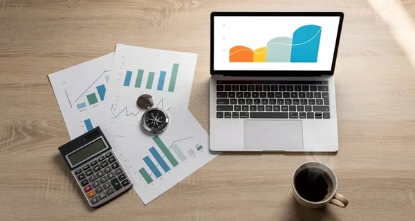 Desk flat lay with a laptop showing a revenue growth chart, printed forecast charts, a compass, and a calculator, representing sales forecasting methods